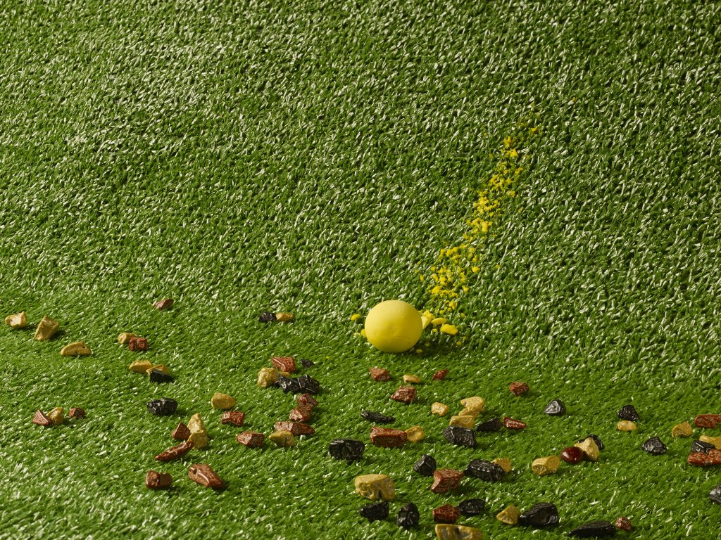 small rock-like objects on green turf next to yellow sphere