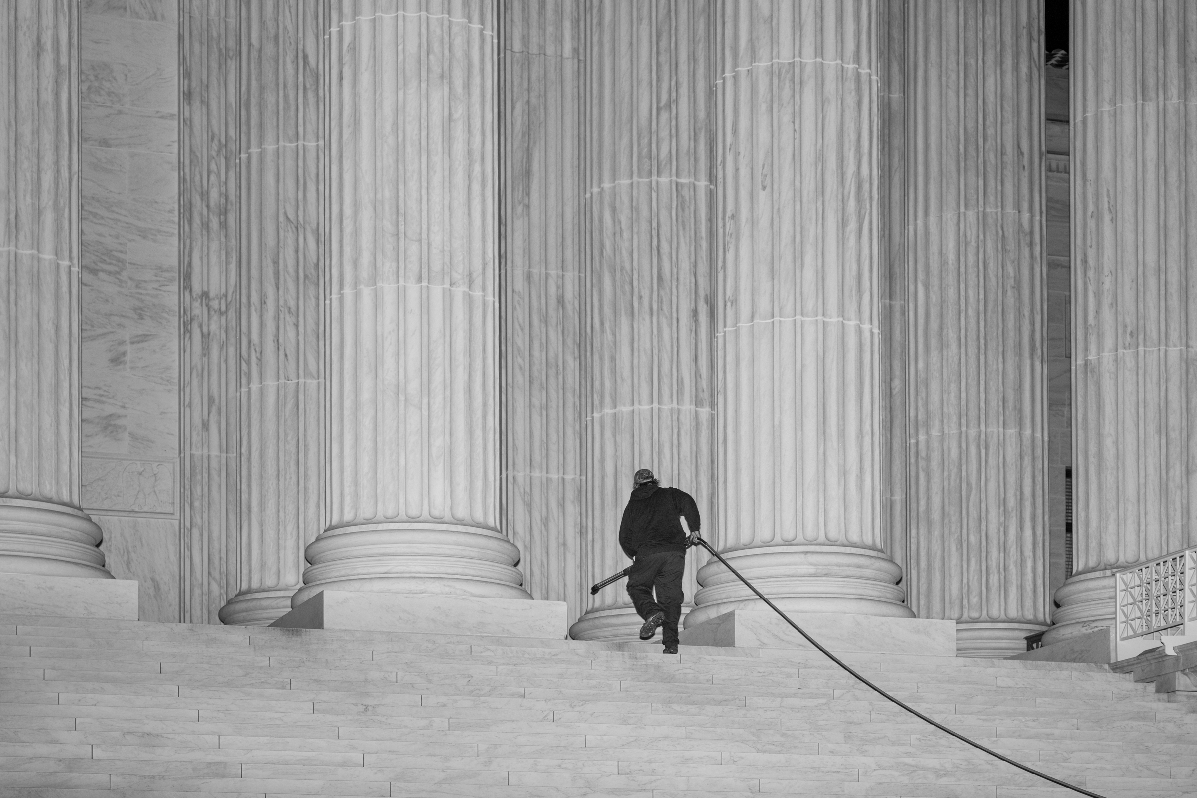 person pulling hose to top of steps at base of building with large classic columns