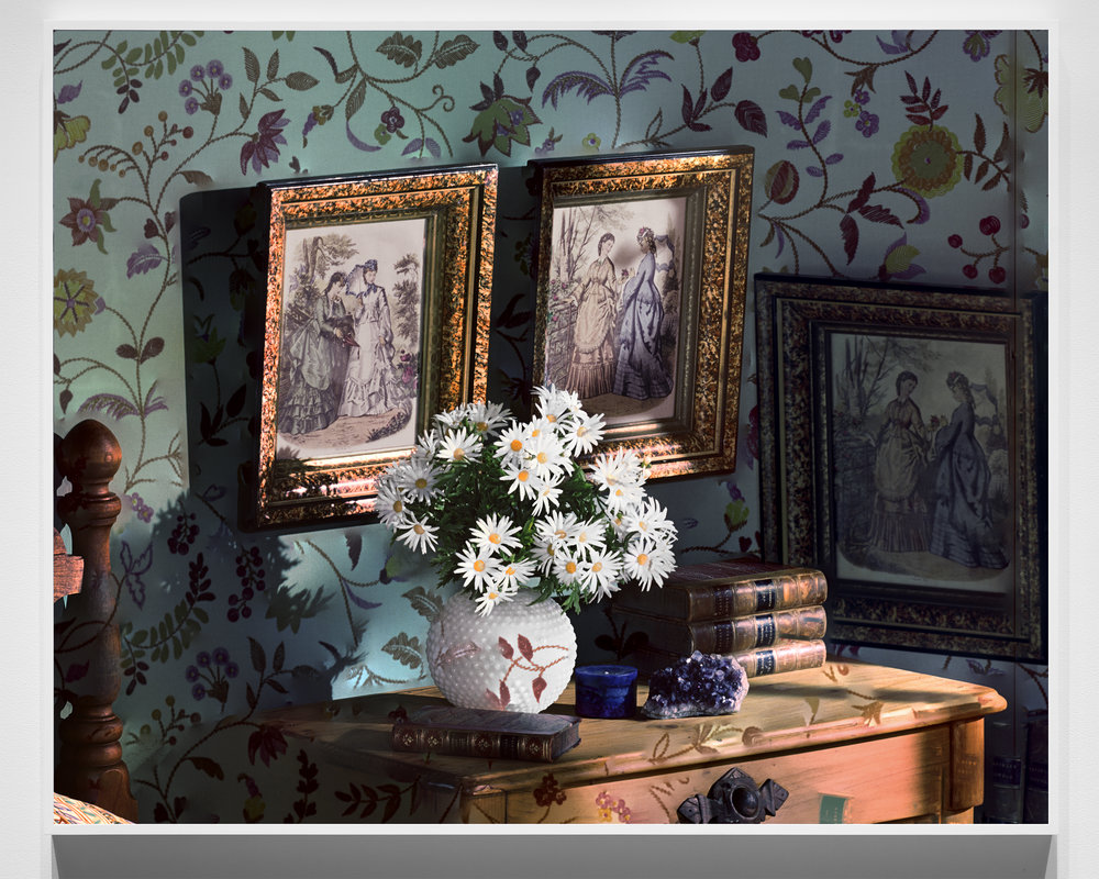 framed photo of historical prints on wall above small side table holding vase of flowers