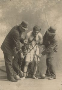 Unidentified photographer, [Harry Houdini in chains and ball weights with police], ca. 1900. Gelatin silver print, 14 x 9.5 cm.