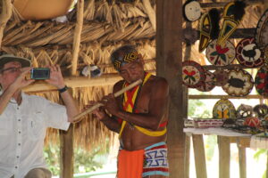 Embera flute player under roof with hand woven baskets behind him, Ted Aanstoos of group 1 in pic - courtesy of Ella Quinlan