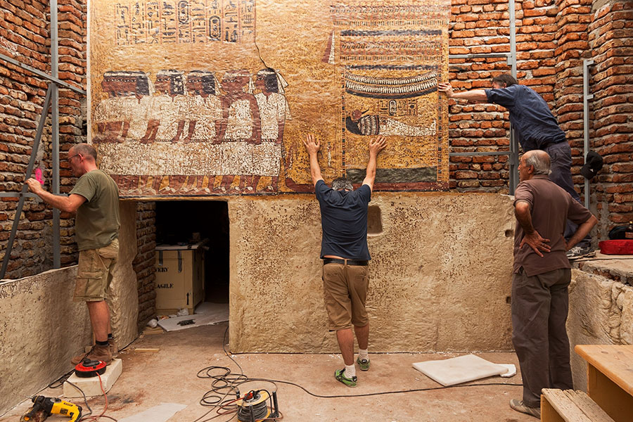 Four people working at archaeological field site interacting with wall mural