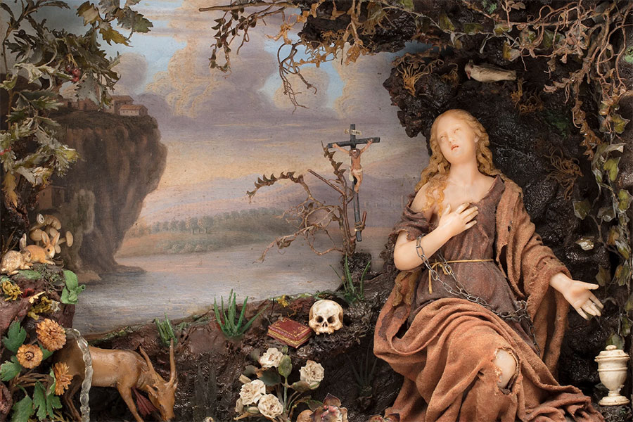 Historic female figure in robes surrounded by objects and a reference to Christ