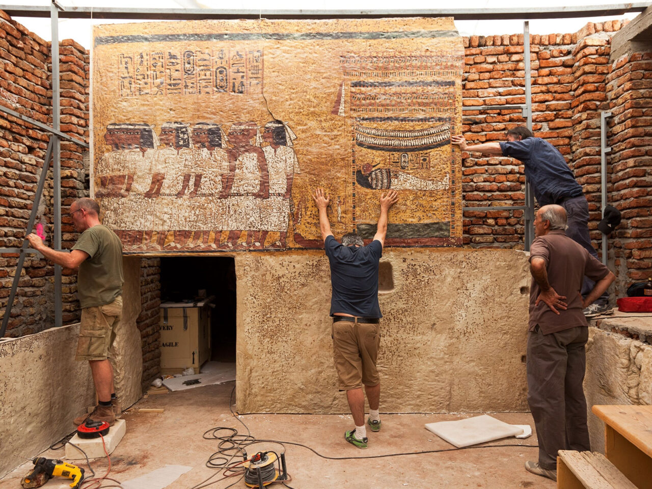 Four people working at archaeological field site interacting with wall mural