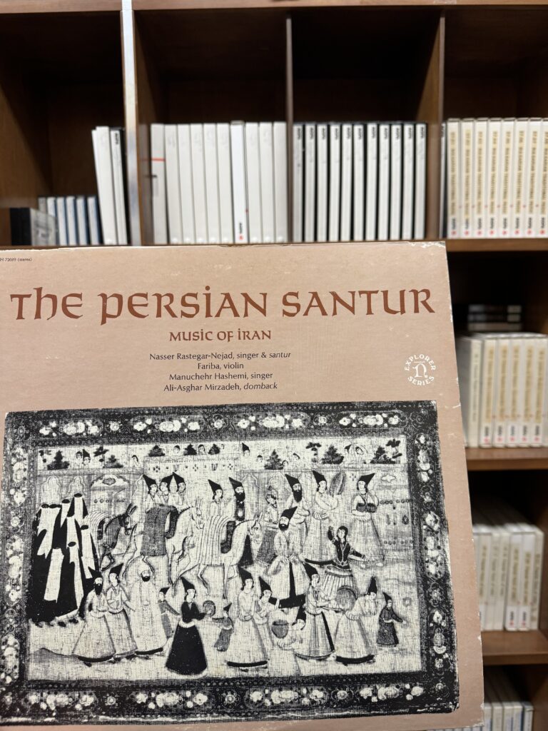 Photograph of a vinyl disc of Persian music, with a group of musicians on the cover art, and 7” tapes in the background