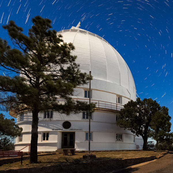 White telescope dome with pine trees and startrails