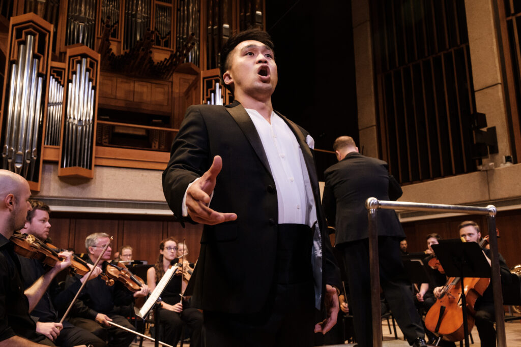Performer stands in front of an orchestra while singing at concert