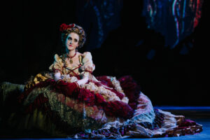Cinderella, wearing a fancy, colorful dress sits on stage looking pensive