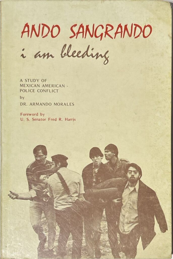 Book cover of Ando Sangrando (I Am Bleeding): A Study of Mexican American-Police Conflict. The book title appears in brown and red. The cover features a photograph of a group of men carrying a person who appears to be injured.