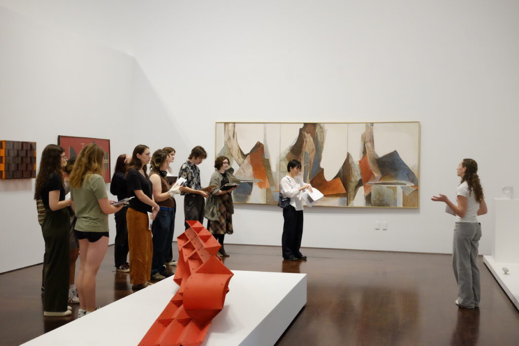 Students visiting a museum holding notes being led by a docent