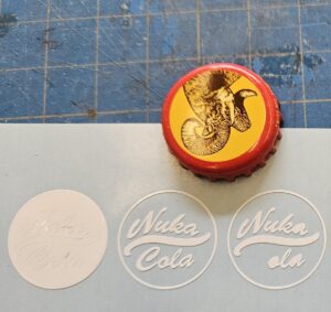 A Shiner beer bottle cap with a ram's head on a yellow background with the words Nuka Cola beneath it