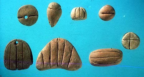 (Fig. 2) Tokens from Tello, ancient Girsu, present day Iraq, ca. 3300 BC. Starting above from left to right : 1 length of textile, one jar of oil, – ? –, one measure of wheat.  Continuing below from right to left: one ram, one length of rope, 1 ingot of metal, 1 garment. Courtesy Musee du Louvre, Department des Antiquites Orientales.