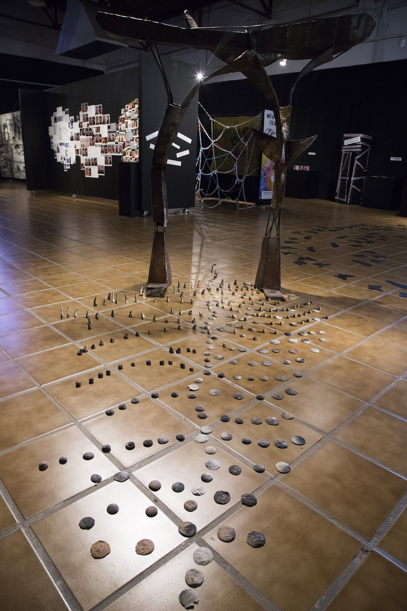 Art installation with large metal sculpture and tokens in pattern along the floor. With gallery and other art in the background.