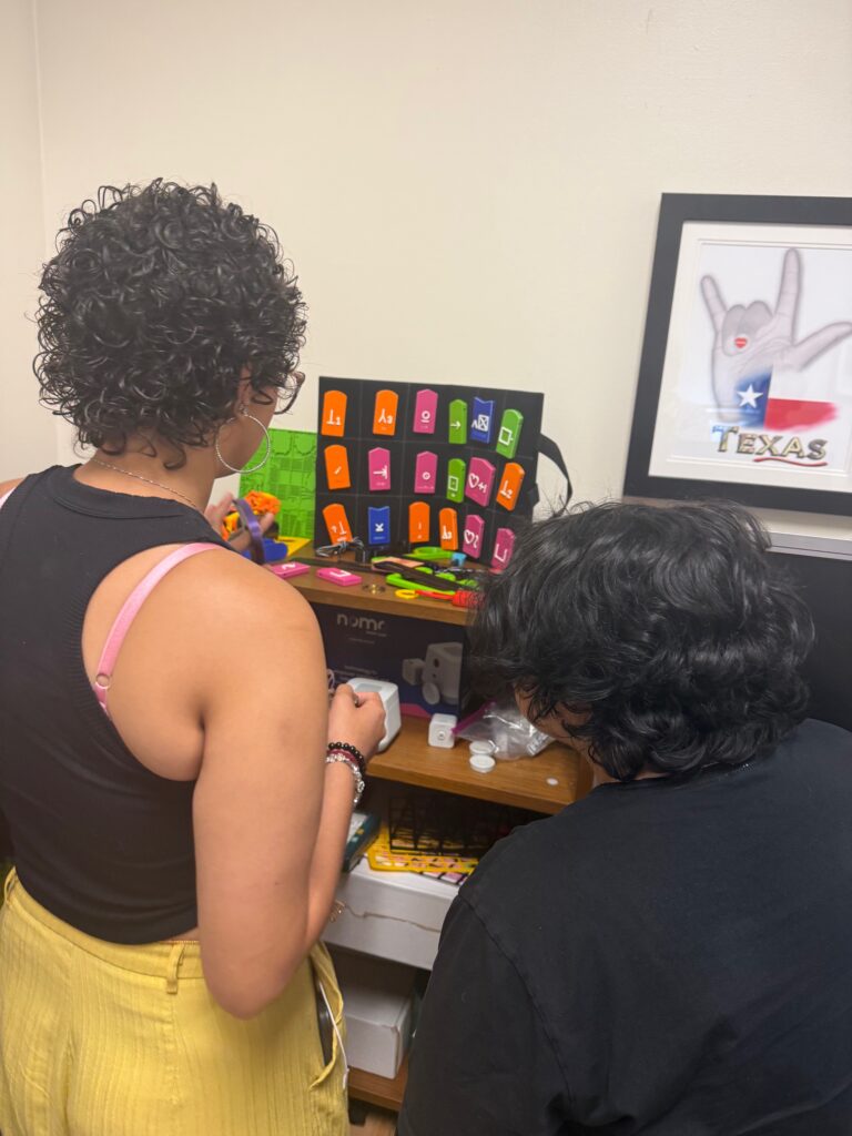 Two college aged students with short black hair photographed from behind looking at brightly colored 3d printed tiles