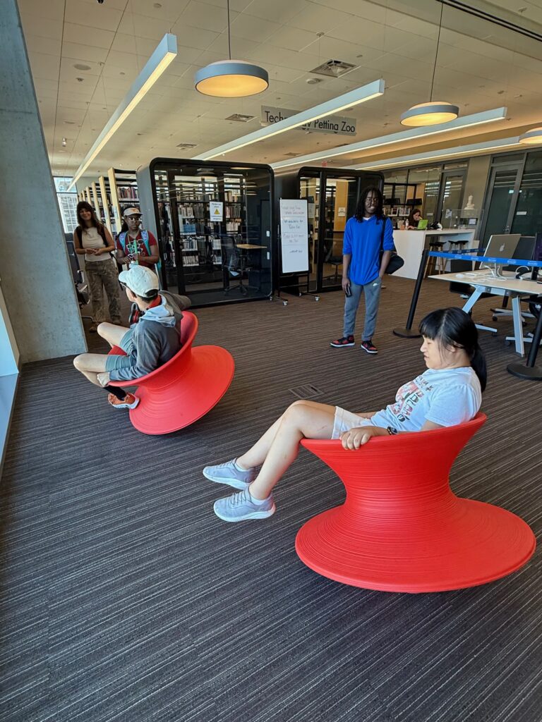 One mixed-race male and one Chinese female student sit in large circular chairs that roll like a top at the Austin Public Library