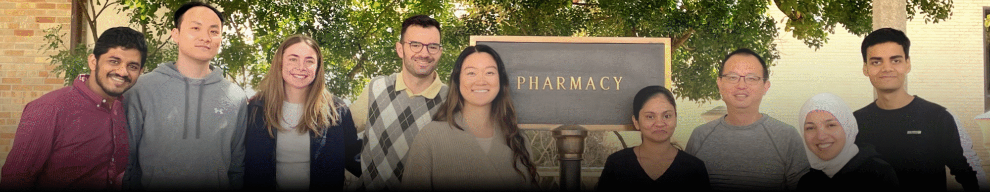 Zhang lab 2025 group photo - all group member standing in front of Pharmacy building sign.