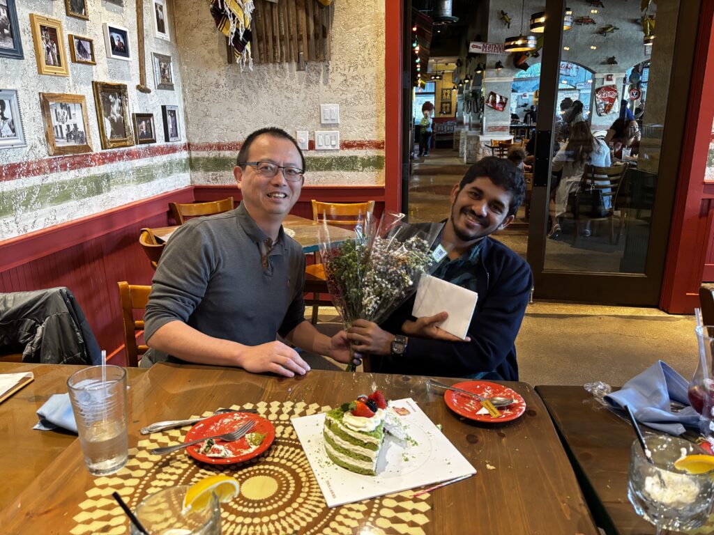 A celebratory moment where Feng Zhang presents a bouquet of flowers to Adwait Pradhan, recognizing their academic achievement (PhD) and new position at Merck.