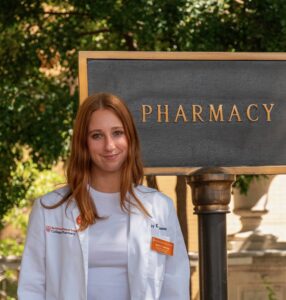 Emily Anderson smiling and standing in front of the Pharmacy Building sign.