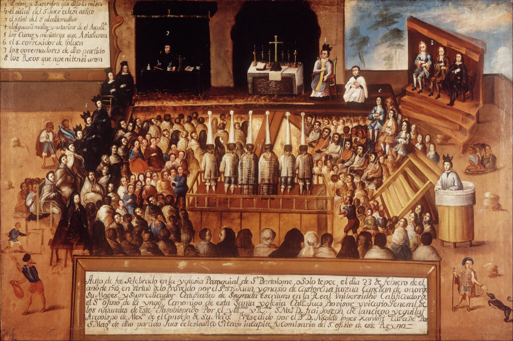 An 18th-century painting shows a courtroom. In the middle, facing away from the viewer, six accused individuals stand on a wooden platform, wearing white conical hats. Many people are seated around them. One man stands and yells at them. On the outer edge, men in black robes sit along the left. At the front of the room is a table with crucifixes and an open book. Two men who appear to be clergy sit near it. In two sections of the painting there are blocks with text in Spanish explaining the scene.