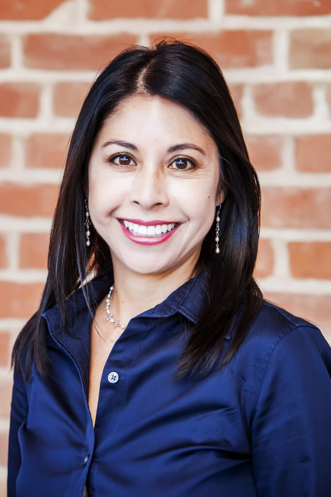 Headshot of a woman with dark brown hair and eyes in a dark-blue shirt who smiles at the camera.