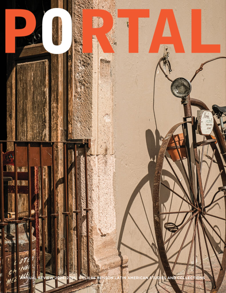 Cover of a magazine showing the front of an old-fashioned bicycle with a large front wheel and curved handlebars, leaning against a beige stucco wall next to a doorway or low window, which is propped open.