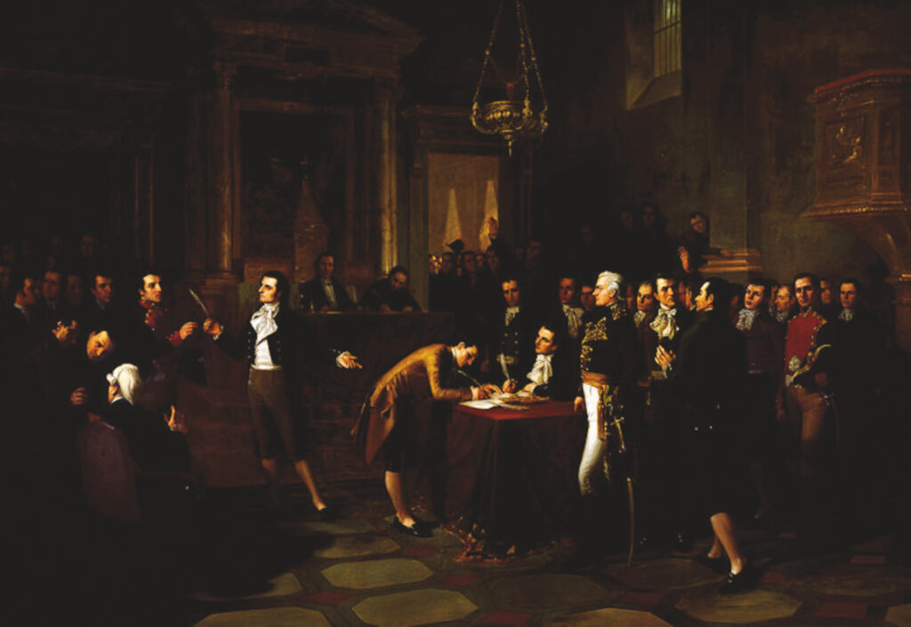A dark oil painting shows the interior of an elegant room with many men in colonial dress. At a table one man is bent over, signing something with a feather pen, while another appears to be sitting at the same table, also signing. One man stands, gesturing at the table and holding a pen.