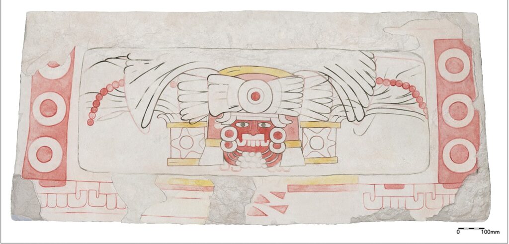 A horizontal slab of white stone is painted in red and yellow, with black outlines, illustrating a storm deity. The fierce face is red, adorned with white earrings and a large headdress and other decorations.