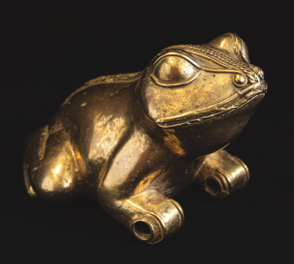 A golden sculpture of a frog against a black background. Most of the surfaces are smooth and round. Features of the face are outlined by twisted or braided gold wire.