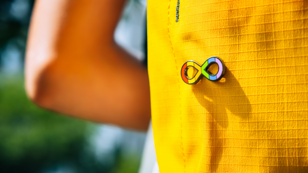 A close up photo of a person wearing an infinity rainbow pin on their yellow backpack