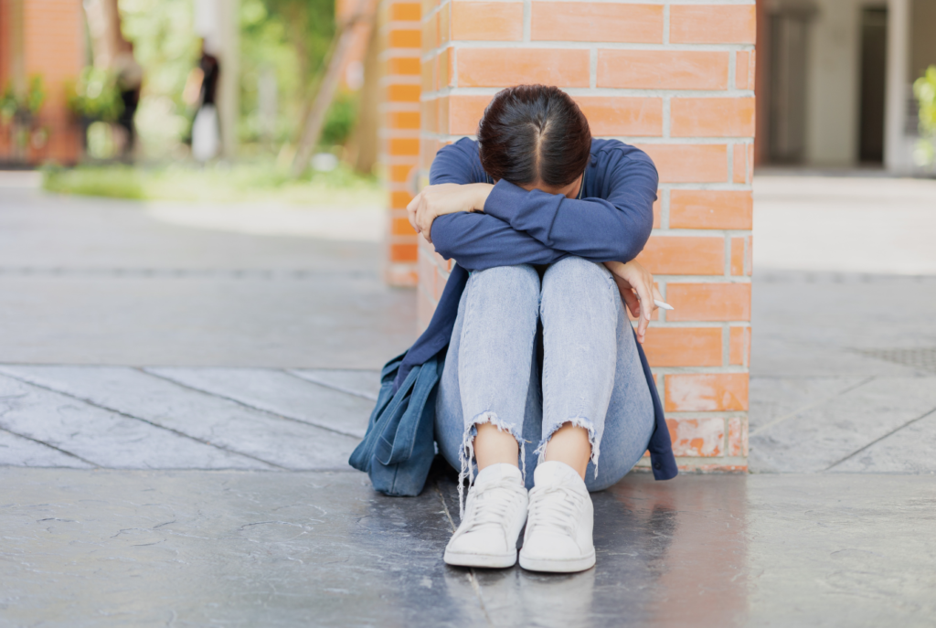 Young student sits on the ground in front of a column with their head down