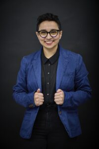 Image of a short-haired person with glasses who is wearing a bright blue blazer and a dark blue shirt