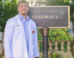 Andy Silva wearing white coat and standing in front of pharmacy building sign