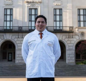 Daniel Flores wearing white coat and standing in front of UT building