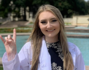 Serra Holthouse wearing white coat and giving hook 'em horns hand sign