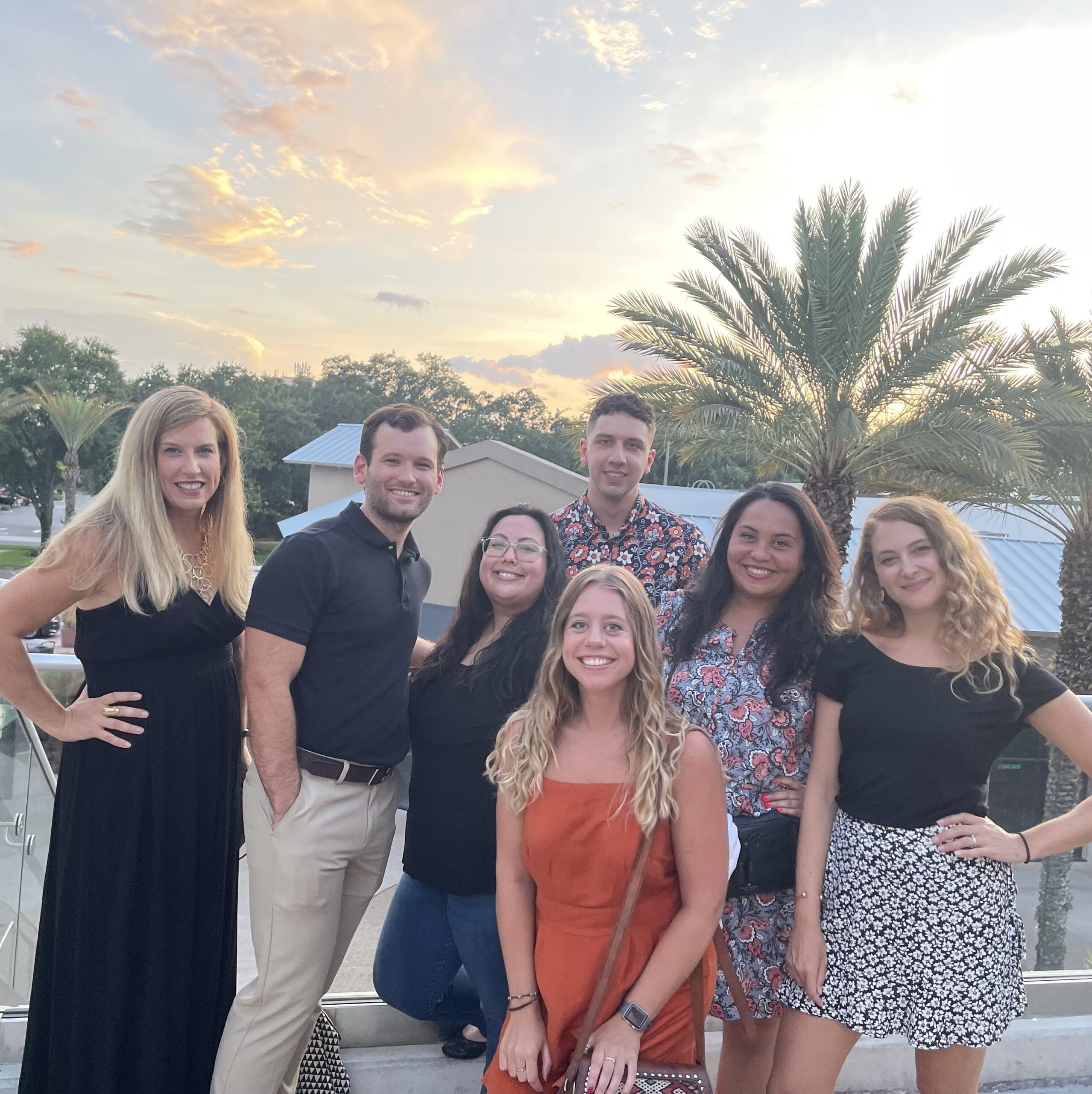 Dr. Nixon and 6 lab members wearing dressy clothes and standing in an outdoor setting with palm trees.