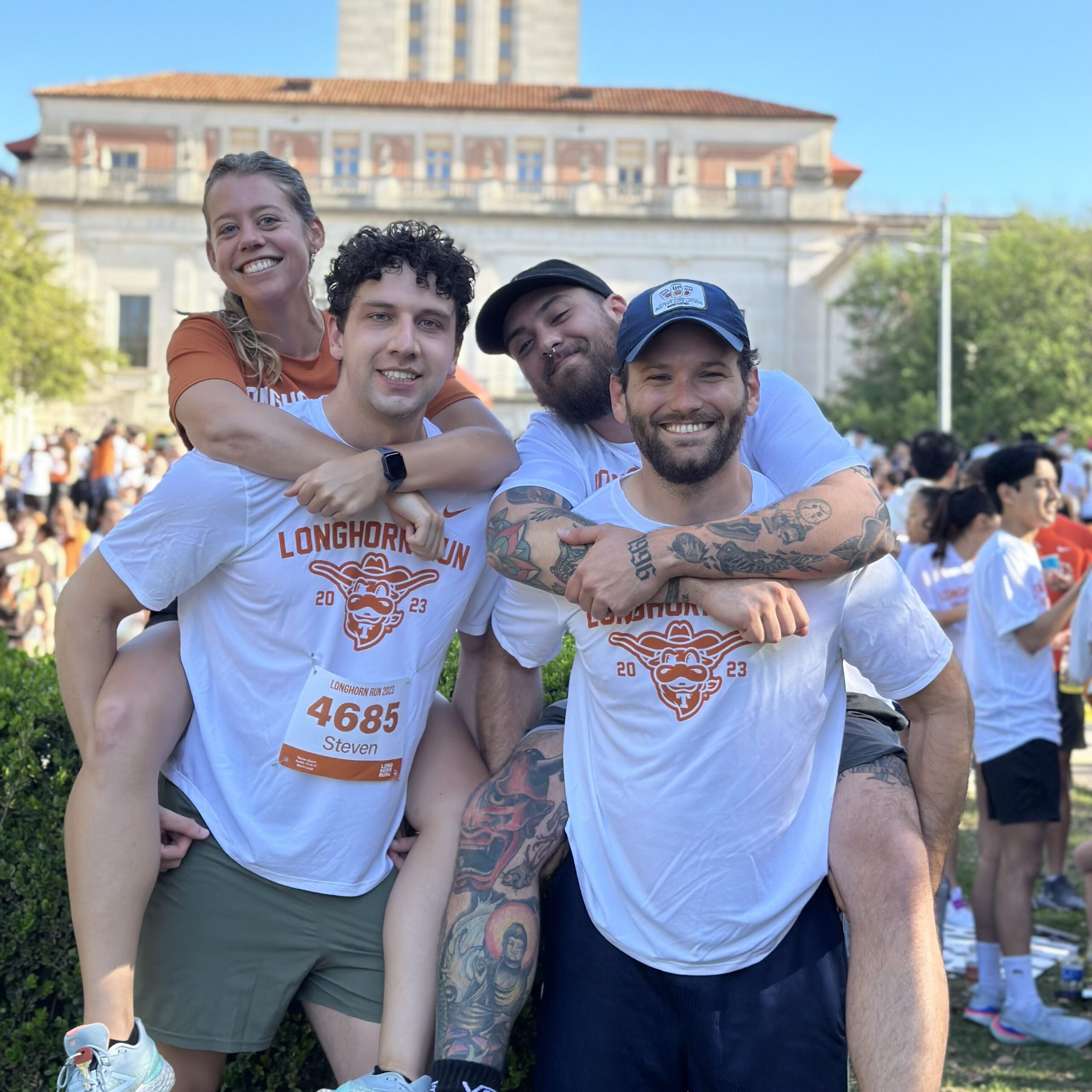 Two lab members giving piggyback rides to two other lab members in front of the UT Tower.  The lab members are wearing race numbers.