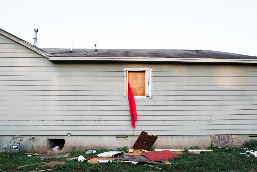 house with boarded-up window holding red fabric