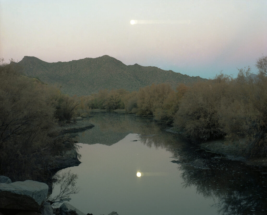 river in desert with bright light above in sky