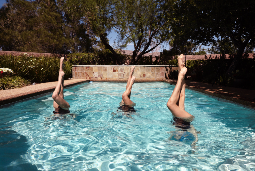 3 women upside down in a pool. 