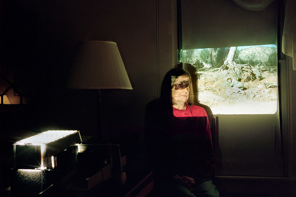person sitting in darkened room, with projector shining light over their head and onto a wall