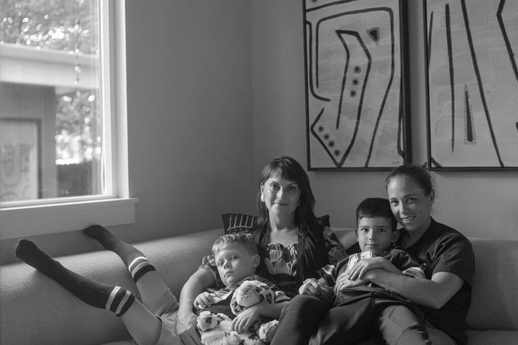 two adults sitting on couch looking at camera, each holding a child