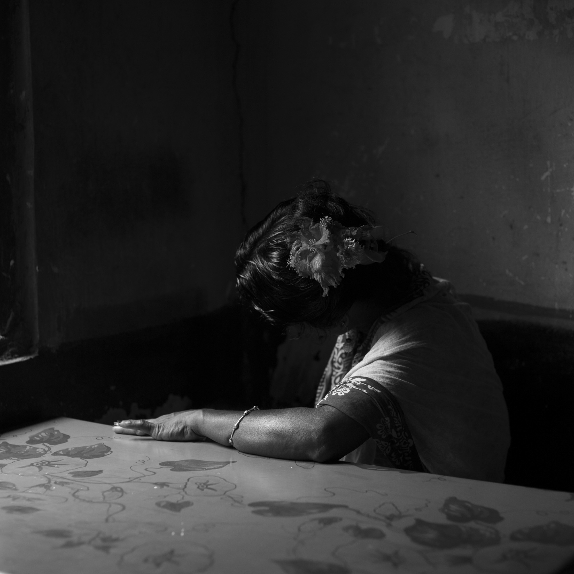 person sitting in darkened room with left arm on table and head down