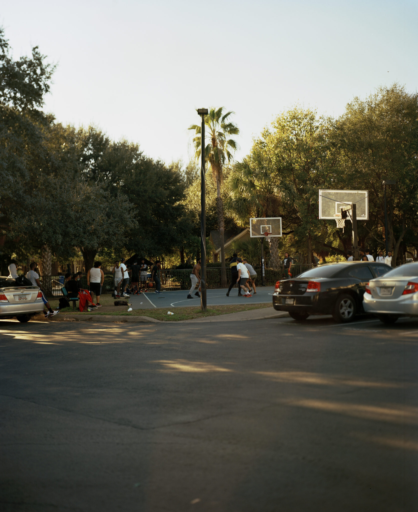 people playing basketball on community court next to parking lot