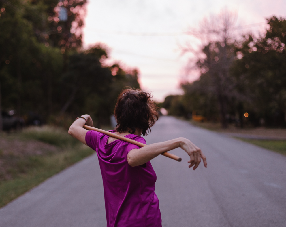 person standing in roadway wearing fuscia short and holding a rod under both arms