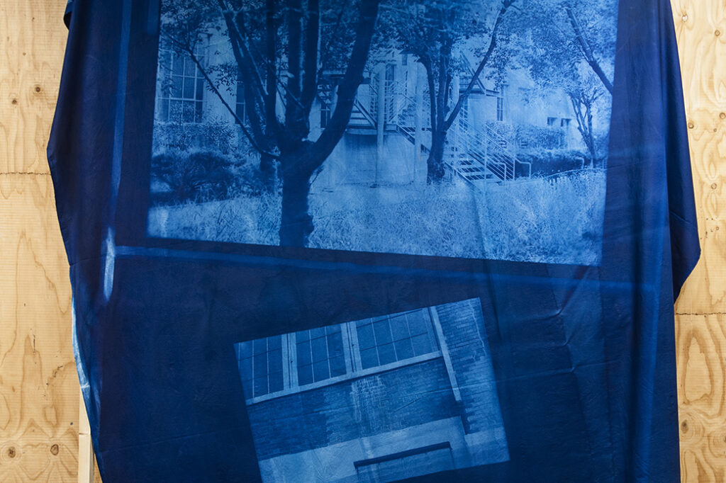 blue fabric printed with two scenes outside of a building draped over a wooden frame set in front of a wall clad in wood