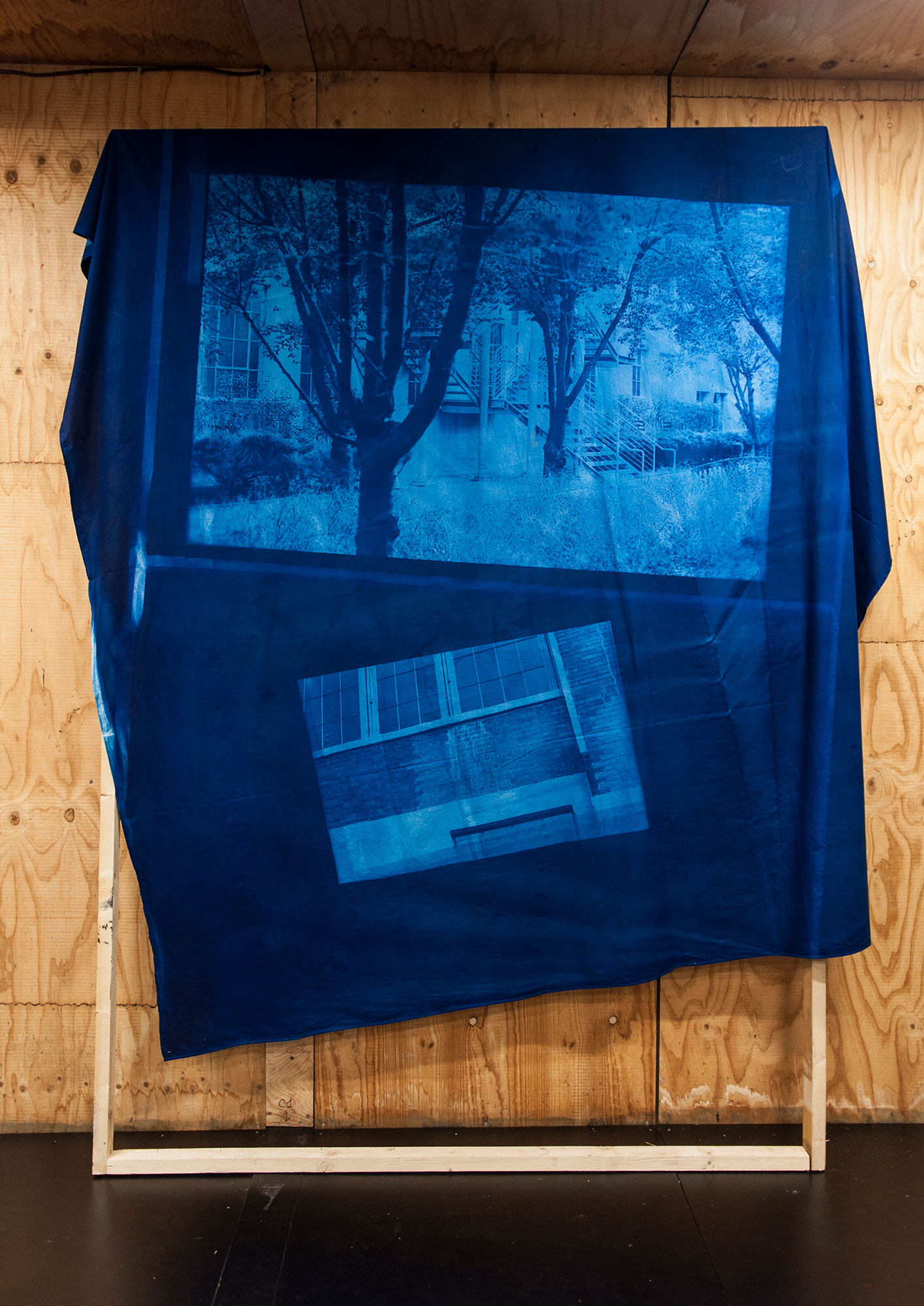 blue fabric printed with two scenes outside of a building draped over a wooden frame set in front of a wall clad in wood