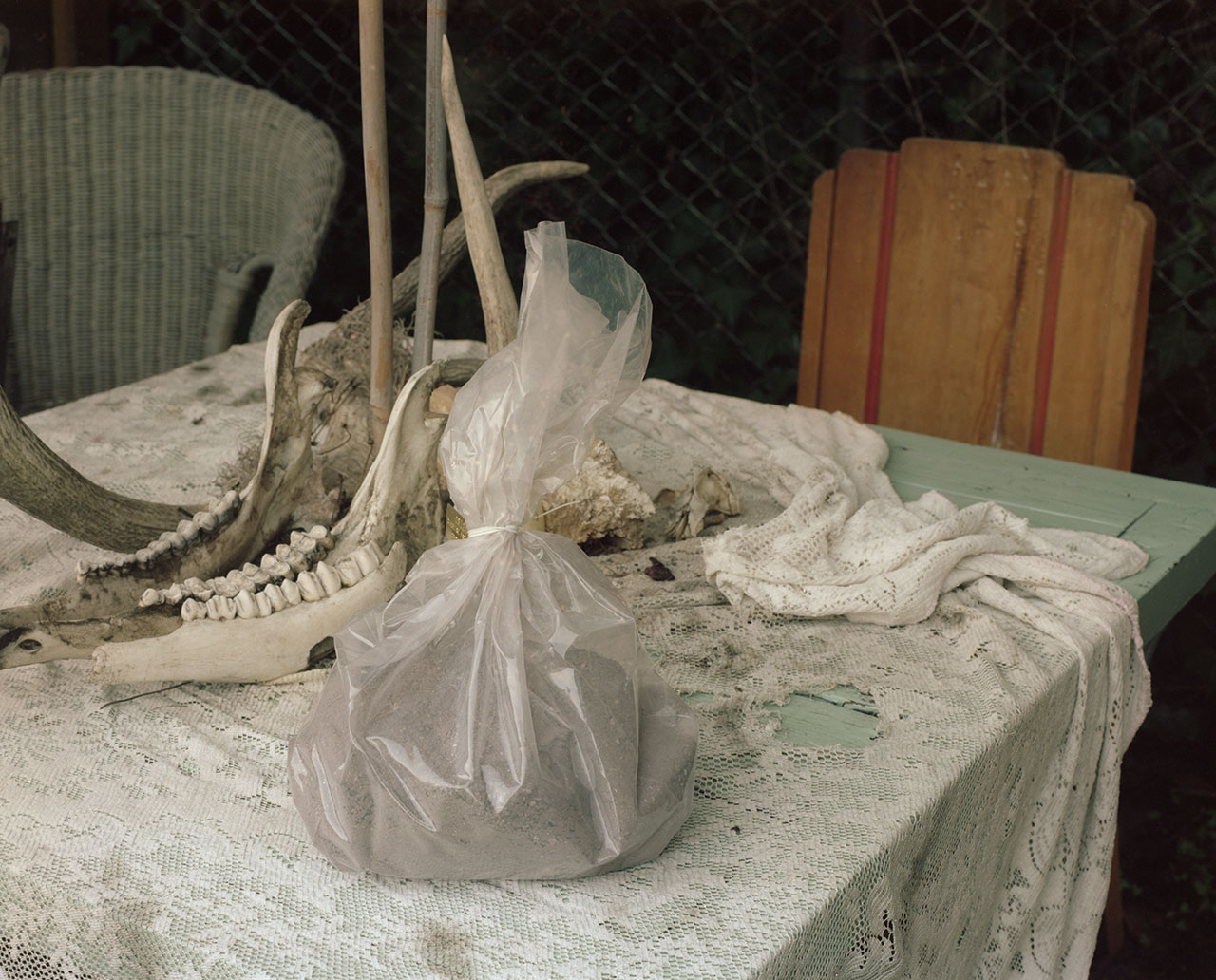 table surrounded by chairs and with objects on top, including plastic bag containing unknown powdery material, jawbone of animal