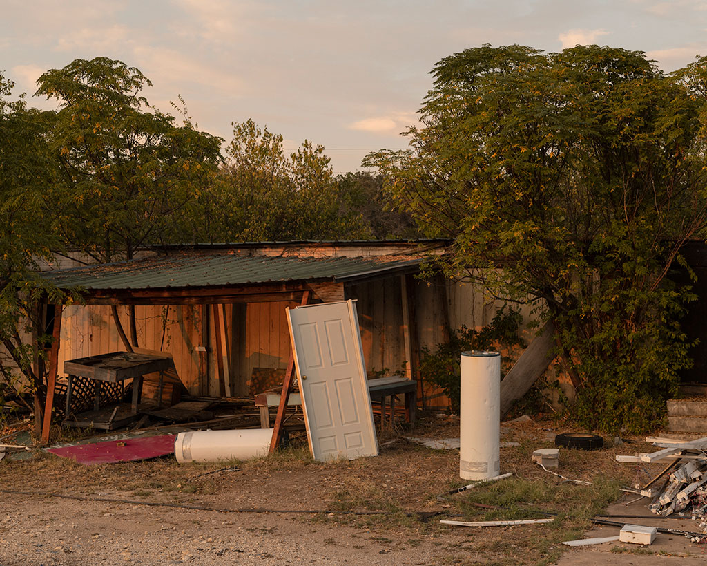 awning on backside of small outbuilding surrounded by construction detritus including a door and water heater tank