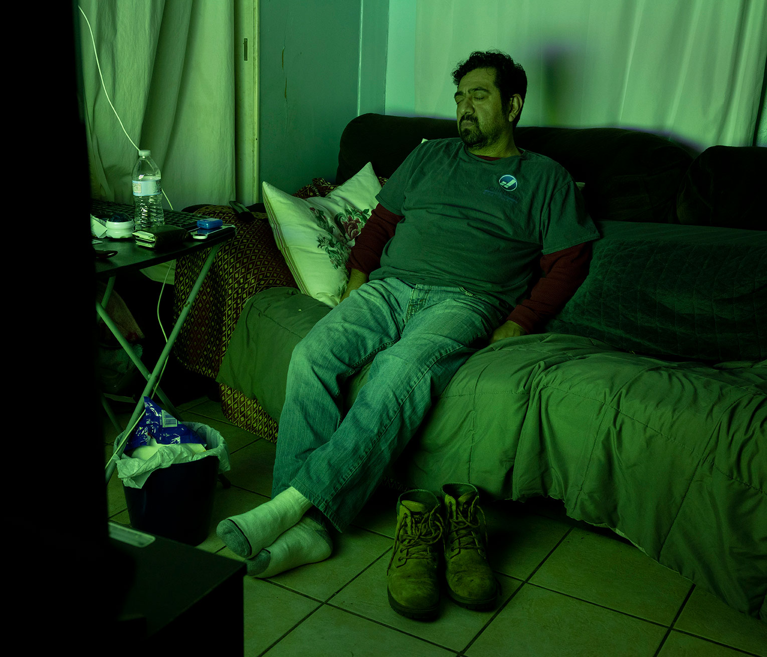 person on couch appearing to sleep with eyes closed in room cast green from television in foreground