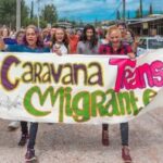 Group of transgender and gay asylum seekers marching down the street holding a large banner that reads "1ra Caravana Trans Gay Migrante...".